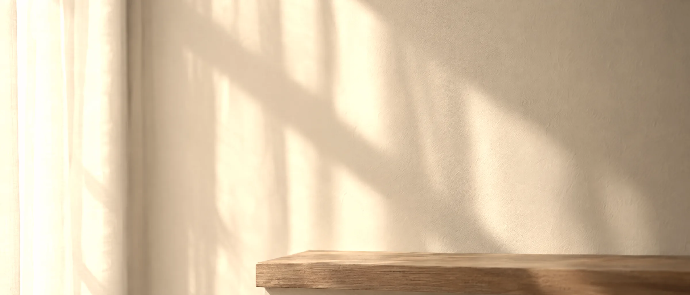 Soft morning light through a sheer curtain falling on a cream kitchen wall above a wooden shelf.