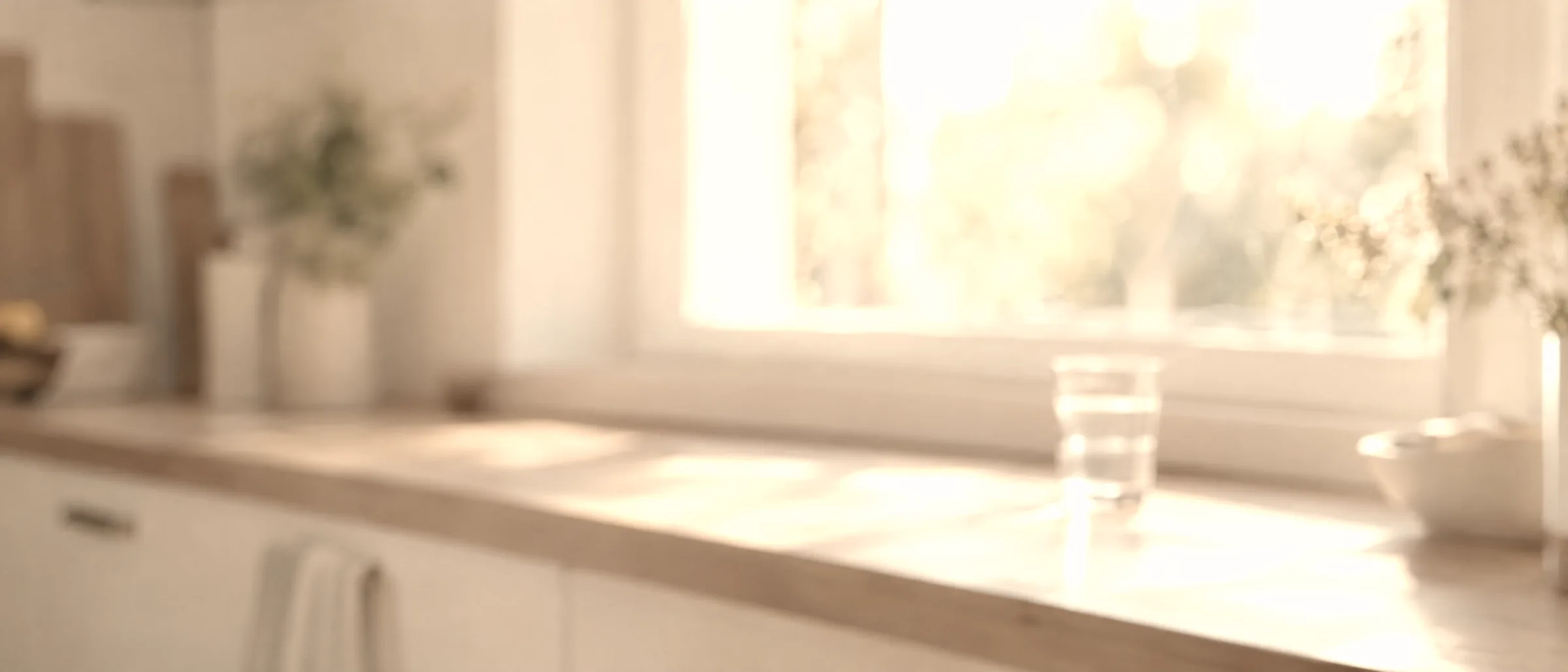 A pale kitchen windowsill with a glass of water, out of focus in bright morning light.
