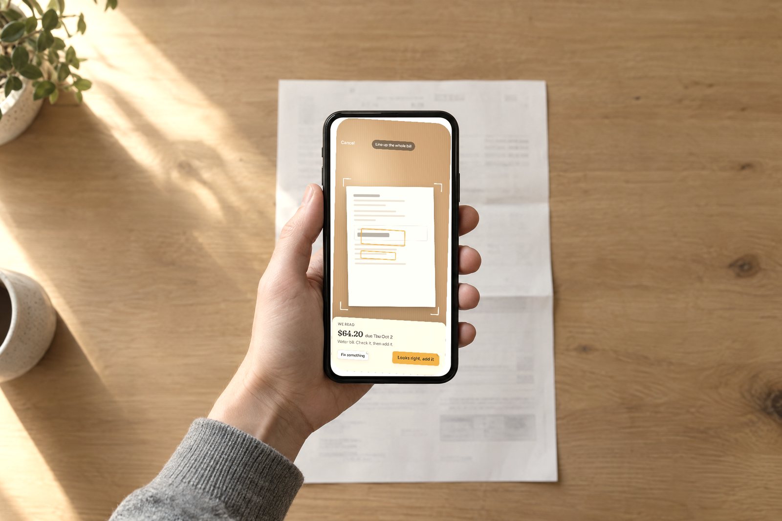 A hand holding a phone above a paper bill on the counter, the Addabill photo capture screen framing the bill and reading $64.20 due Thu Oct 2.